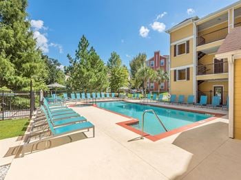 One of two sparkling swimming pools with teal lounge chairs surrounding the pool deck at Evergreens at Mahan apartments for rent